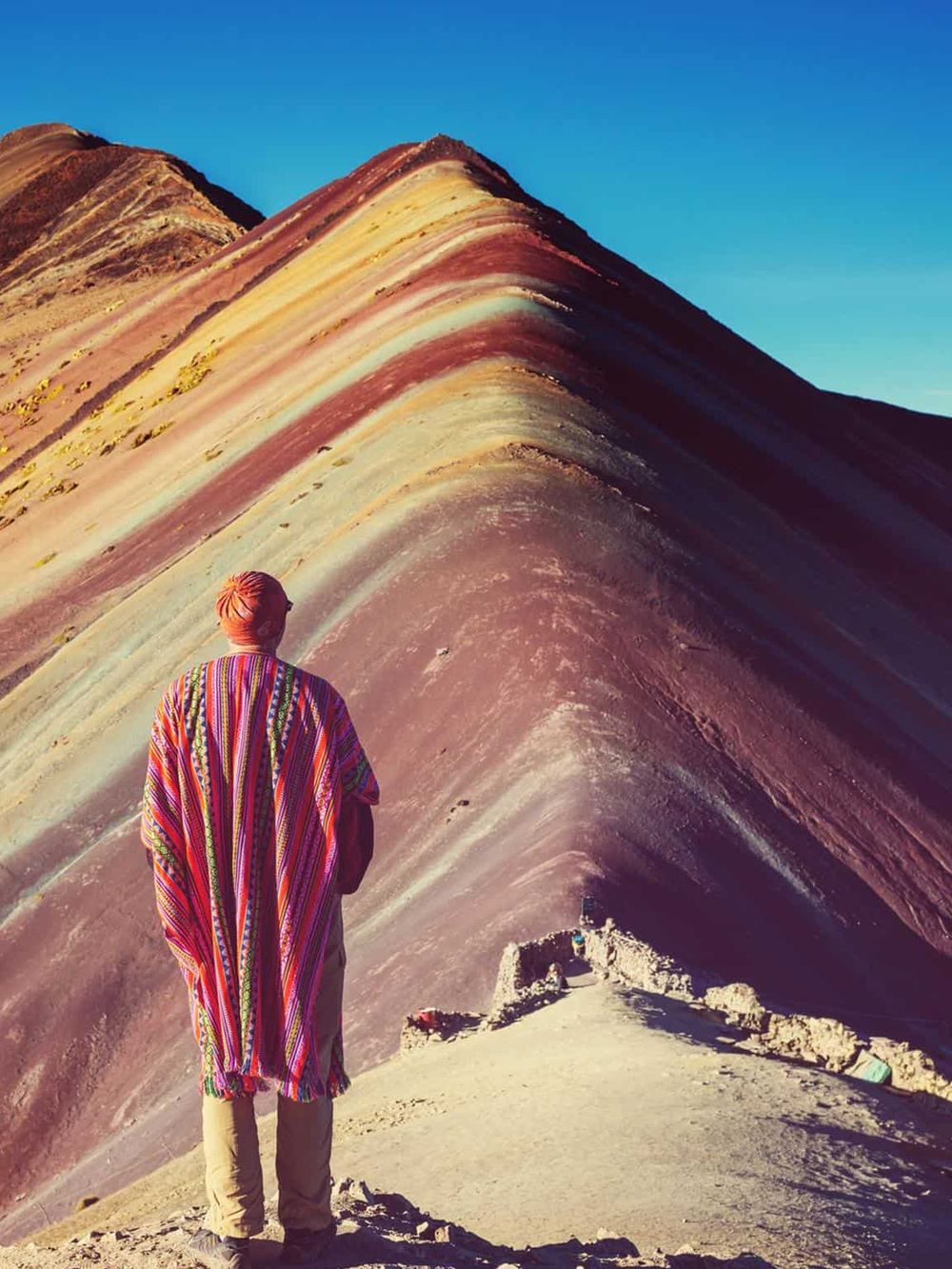 Vibrant rainbow mountain landscape with traveler wearing colorful traditional attire exploring Peru's scenic highlands.