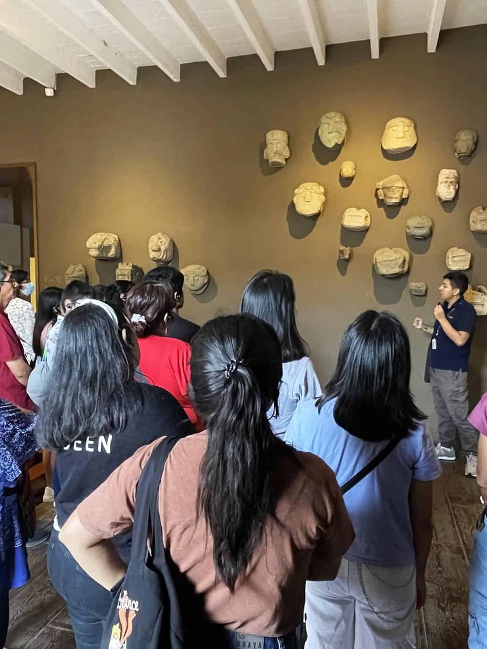 Ancient Mesoamerican stone masks display at museum, guided tour in progress, educational cultural experience.