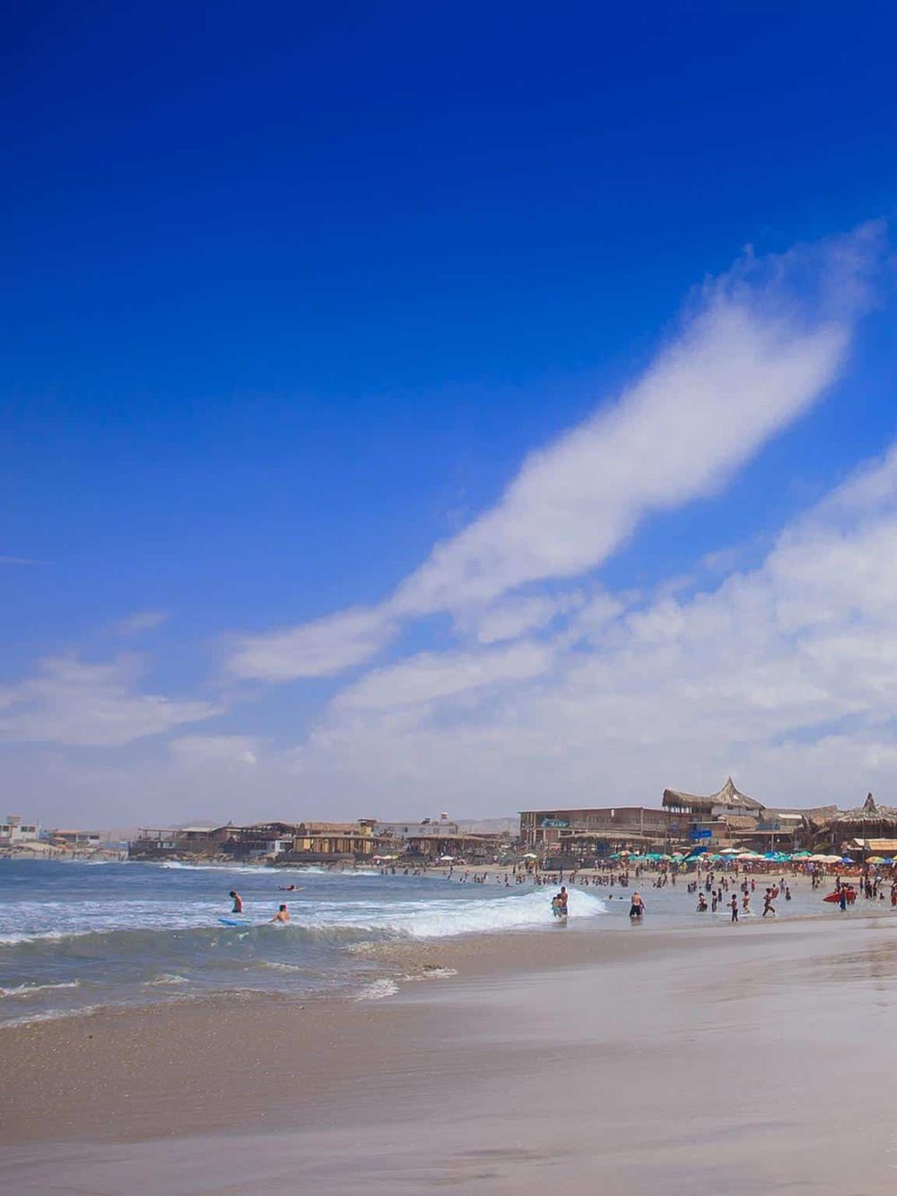Beautiful beach scene with blue sky, ocean, and crowds enjoying the seaside.