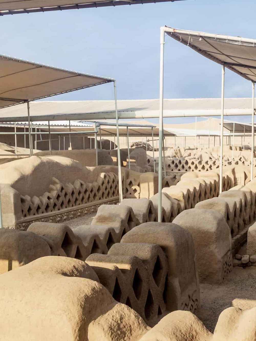 Ancient stone structures with intricate carvings under shade canopies, showcasing historical archaeological remains.