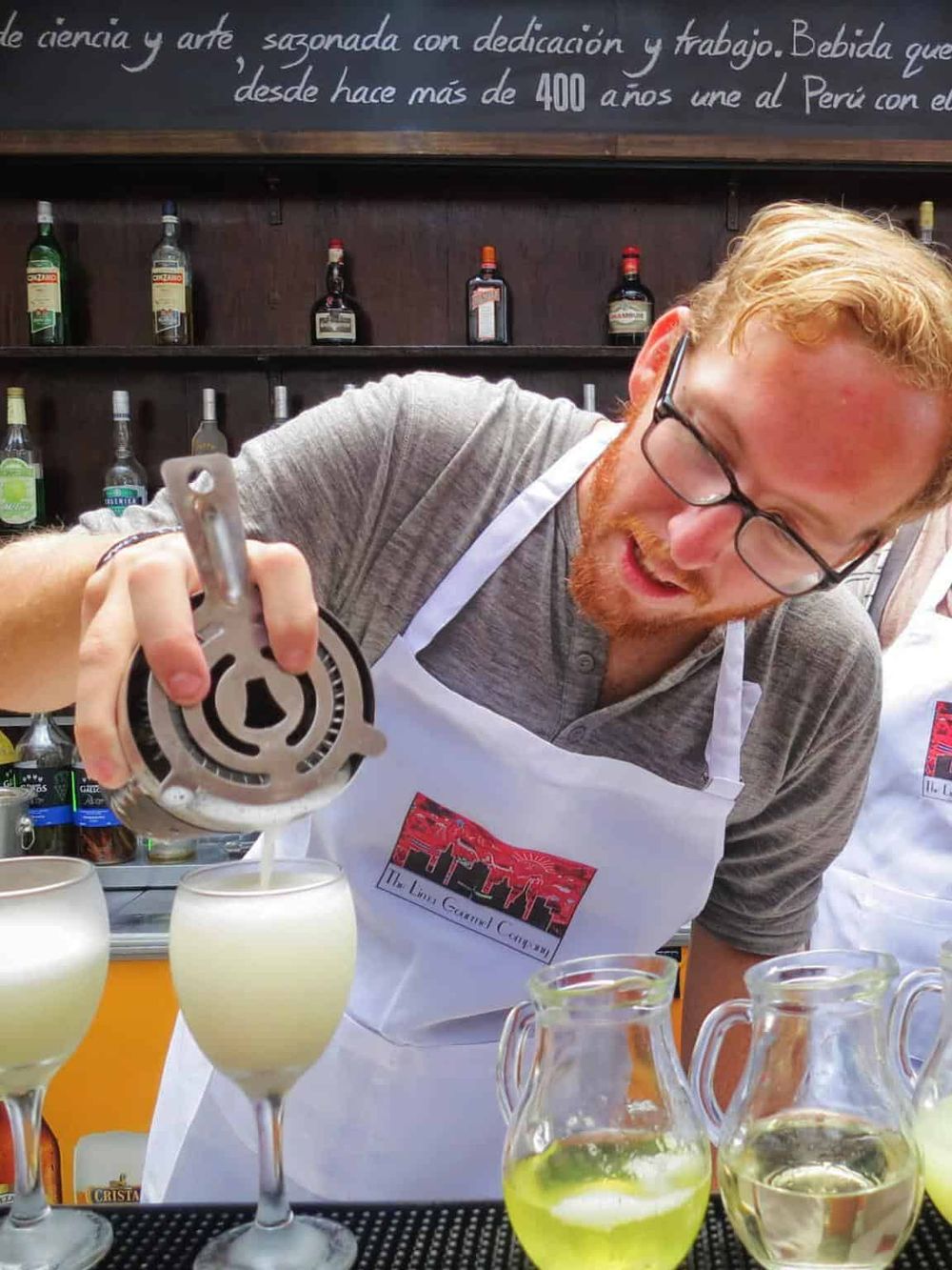 Refreshing alcoholic beverages being prepared at a bar with a bartender pouring drink, surrounded by bottles and colorful glasses.