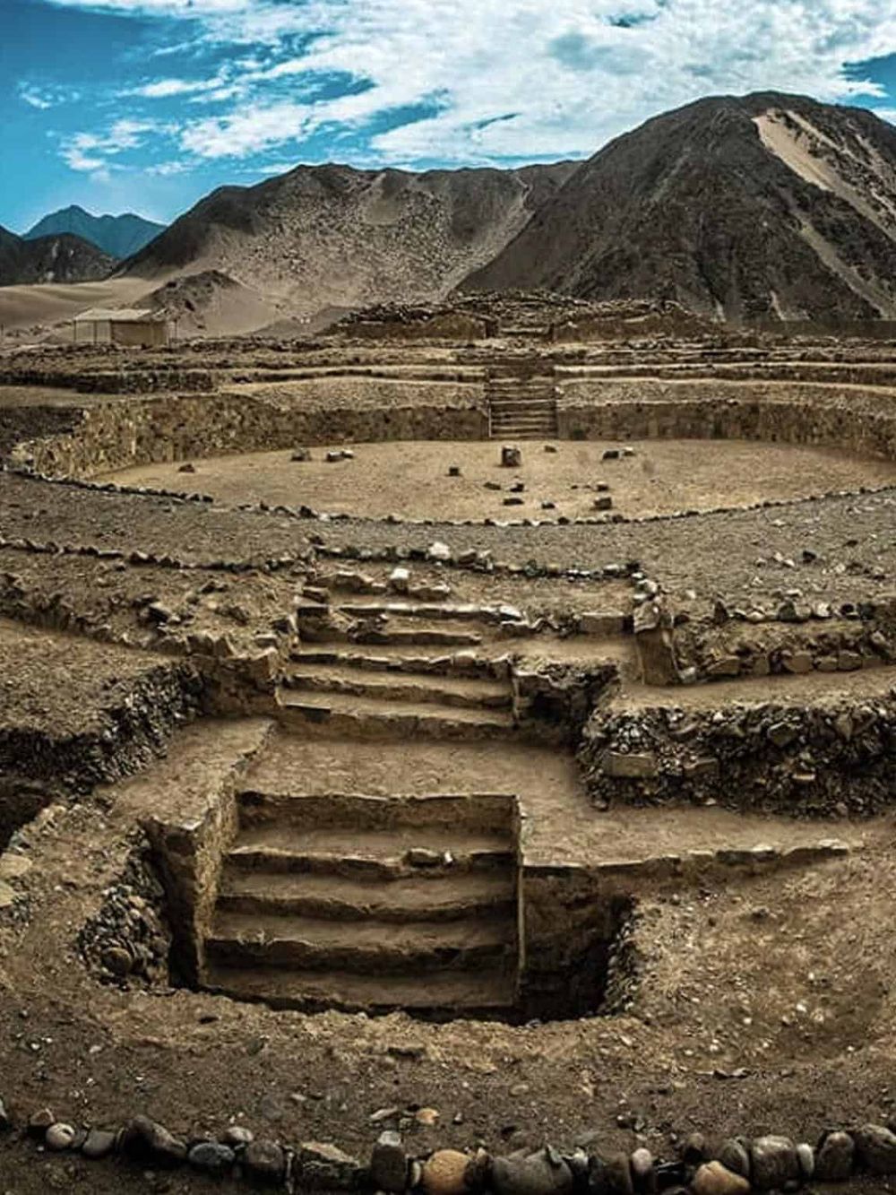 Ancient archaeological site with terraced structures and mountain backdrop, serene desert environment, historical exploration, and adventure.