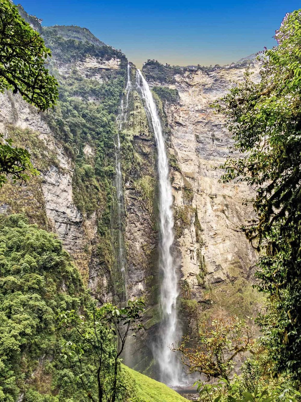 Waterfall in lush green forest with cascading stream and rugged cliffs, scenic natural beauty.