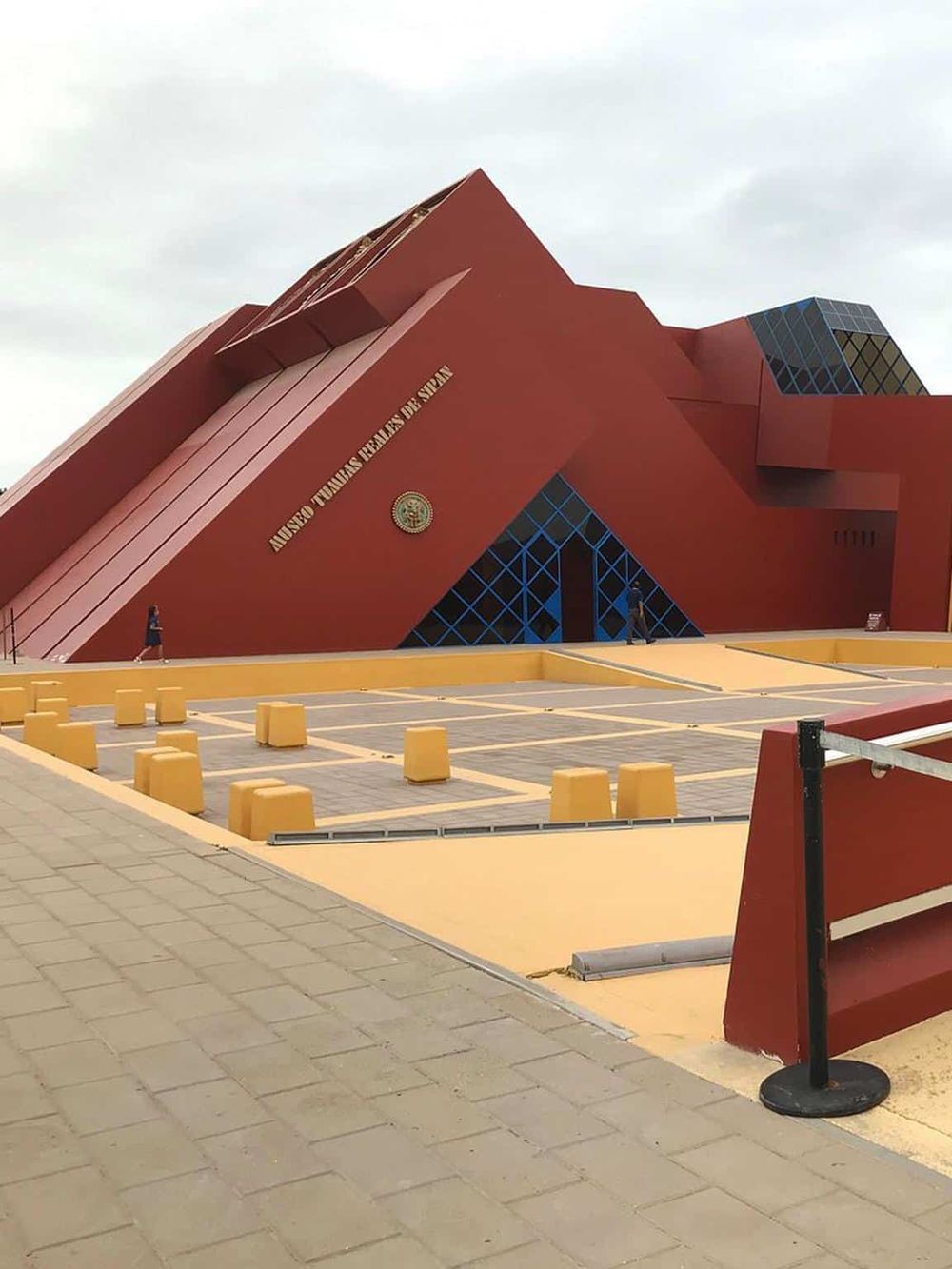 Modern Mexican government building with innovative architecture, red exterior, and surrounding plaza with seating.