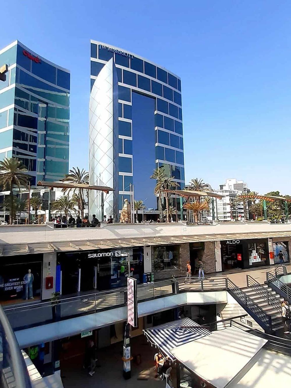 Modern office building with reflective glass exterior and bustling retail space below, located in a lively urban shopping district.