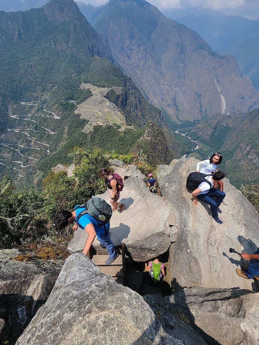 Aerial view of hikers climbing a rocky trail on Machu Picchu mountain, with lush terraced landscape below.