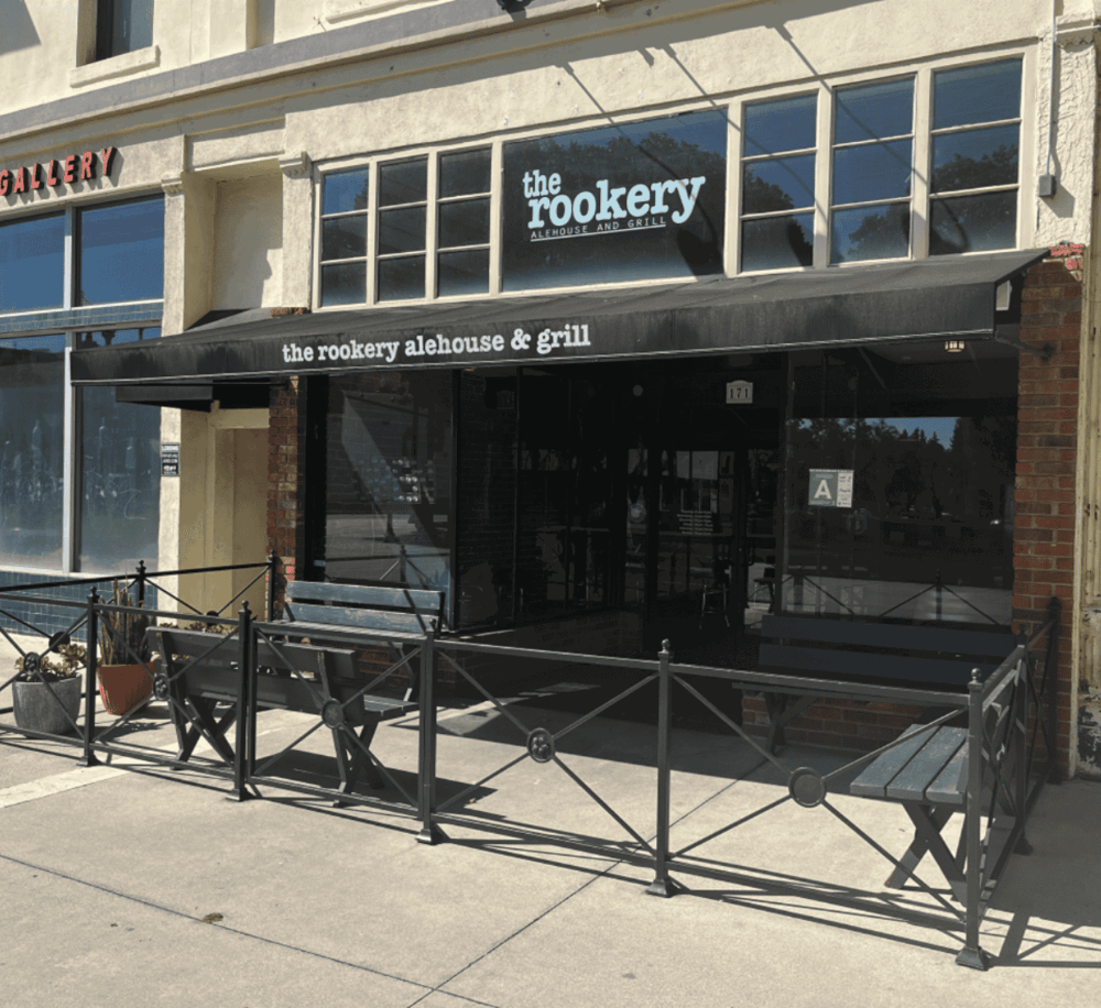 Cozy gastropub exterior at The Rookery Alehouse & Grill with outdoor seating and black awning.