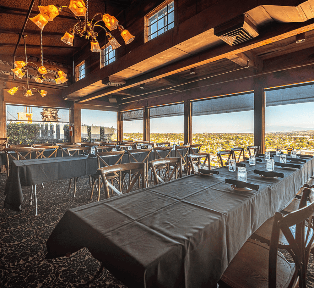 Cozy restaurant with large windows offering scenic city views, elegant lighting, and black table settings.