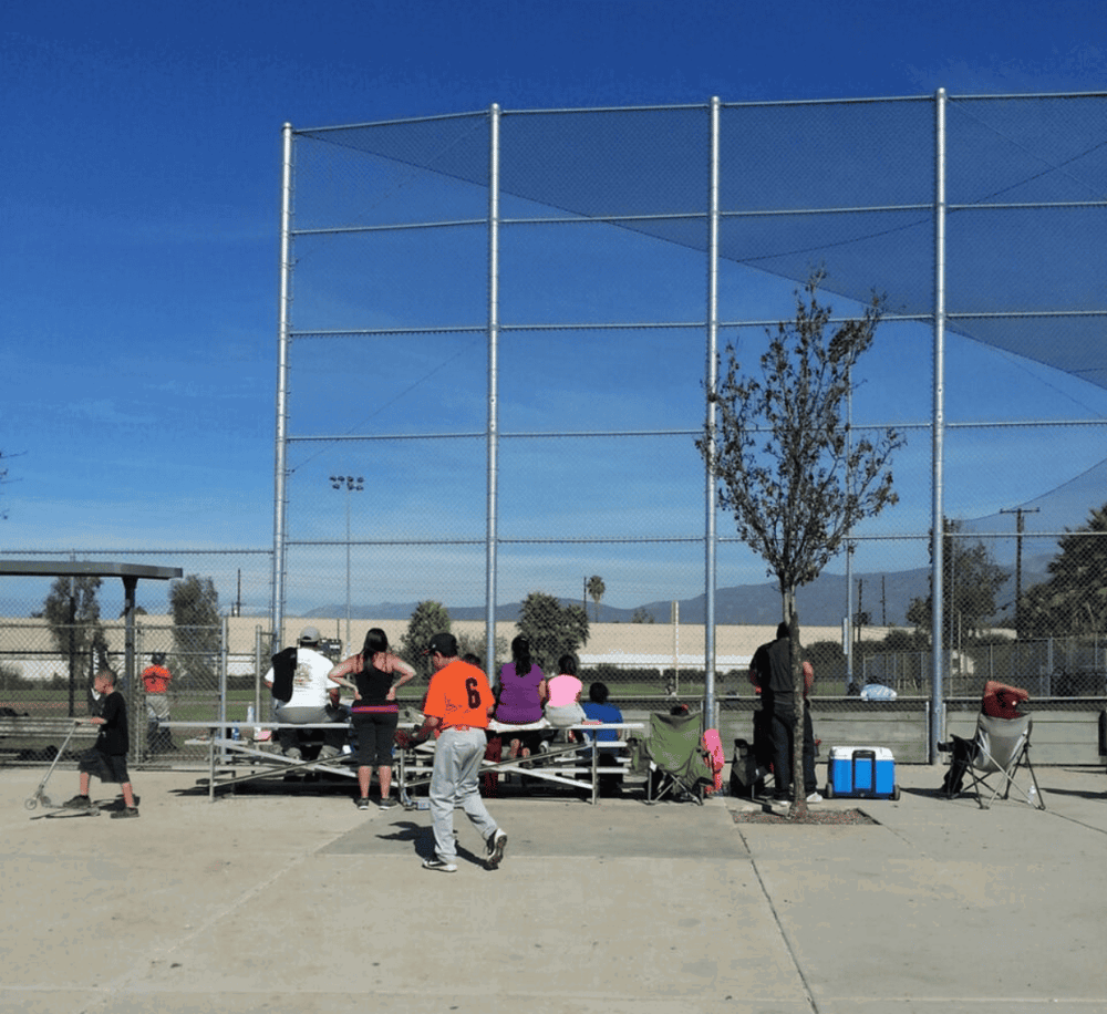 Children and adults at a baseball field bleachers during daytime with blue sky.