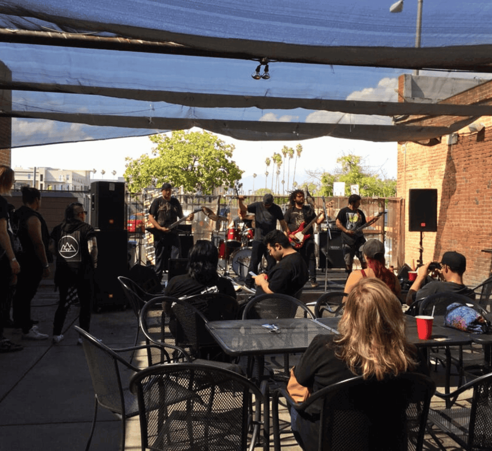 Live outdoor concert with a band performing under a shaded patio, outdoor venue, live music event, QuestForDirections.