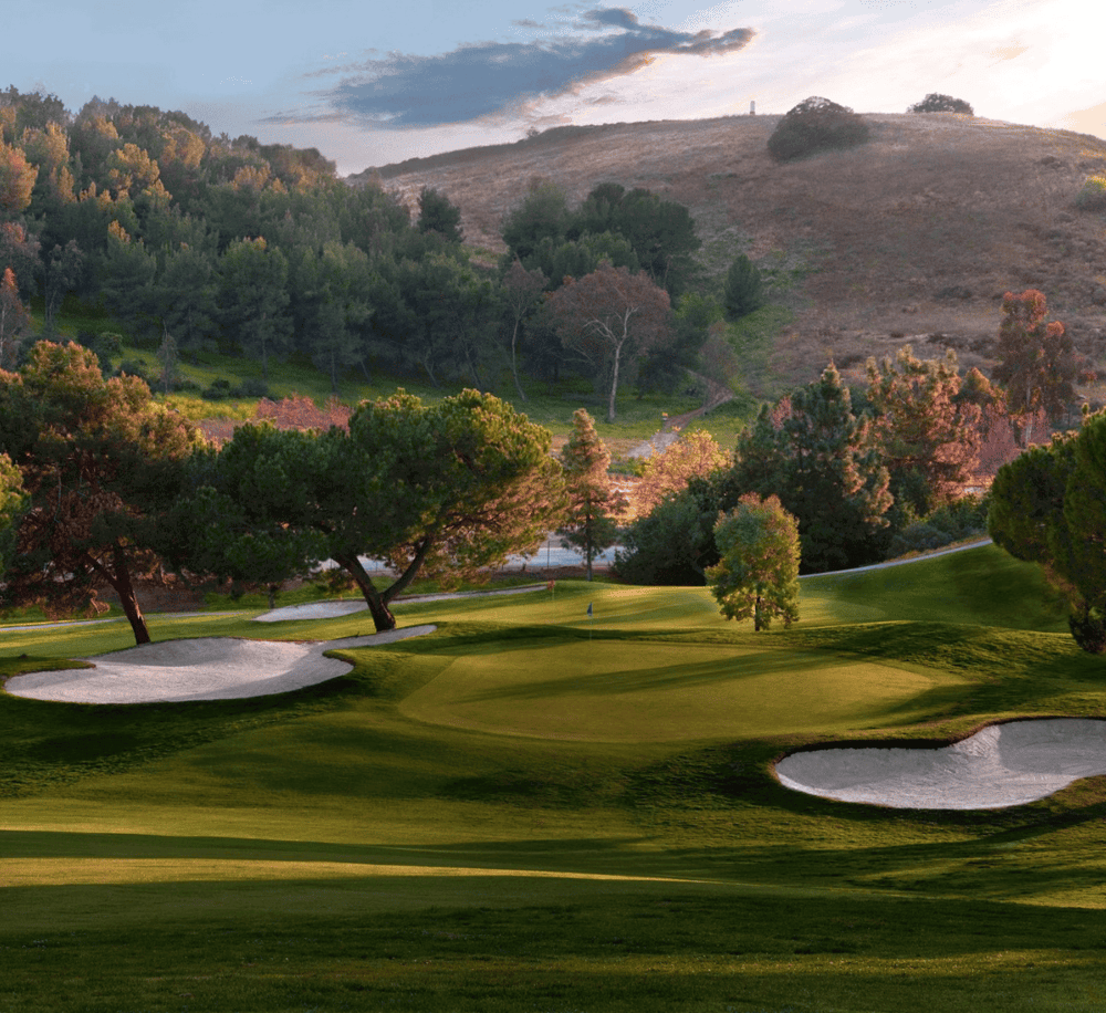 Lush golf course with sand traps and scenic mountain backdrop at sunset.