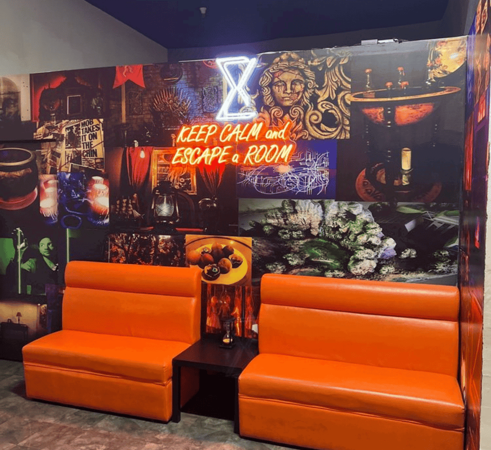 Vibrant escape room lounge with neon sign, bold wall art, and comfy orange seating for immersive adventures.