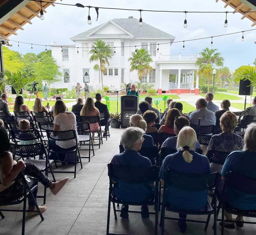 Engaging outdoor event at a stylish venue with audience, stage, and scenic white house backdrop.