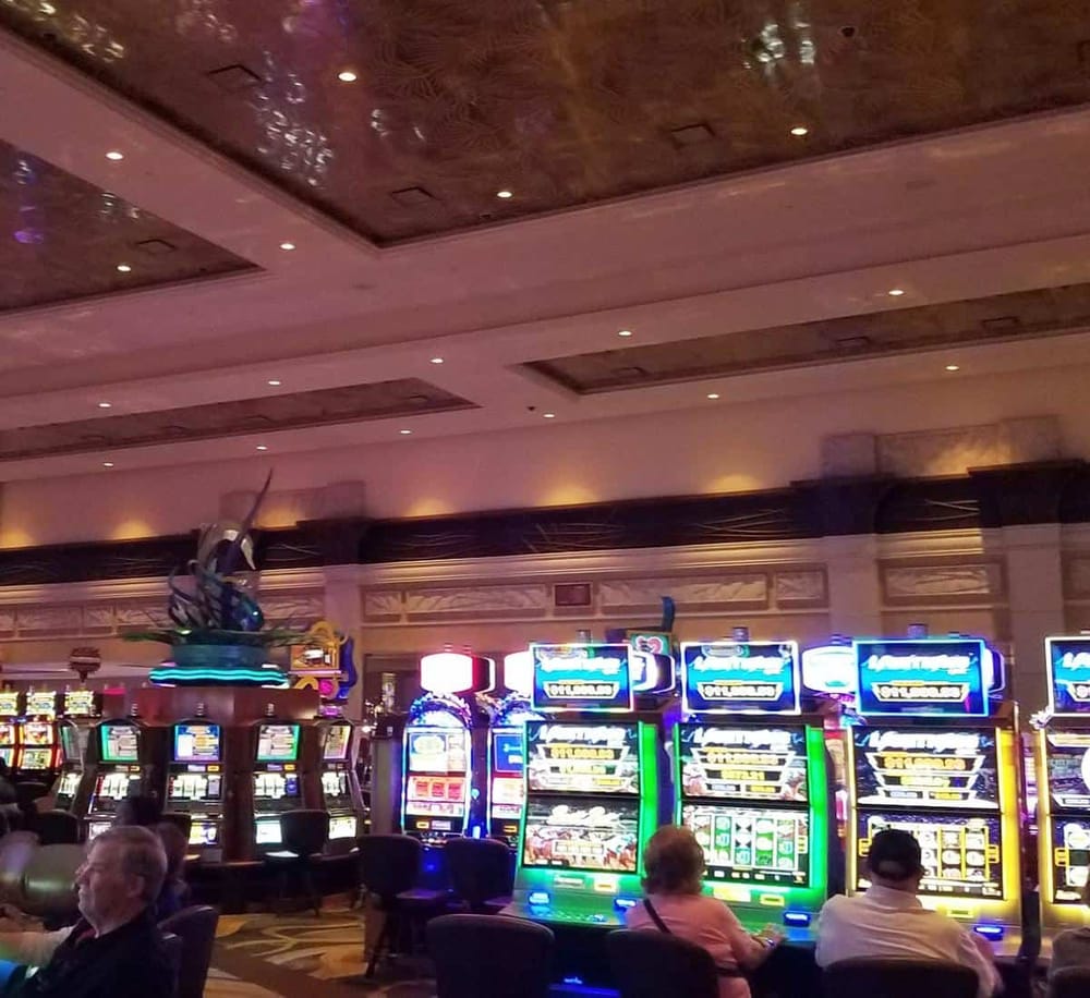 Brightly lit casino with slot machines and people playing, colorful lights, and a luxurious interior.
