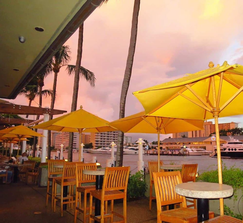 Bright marina restaurant patio at sunset with yellow umbrellas and wooden tables.