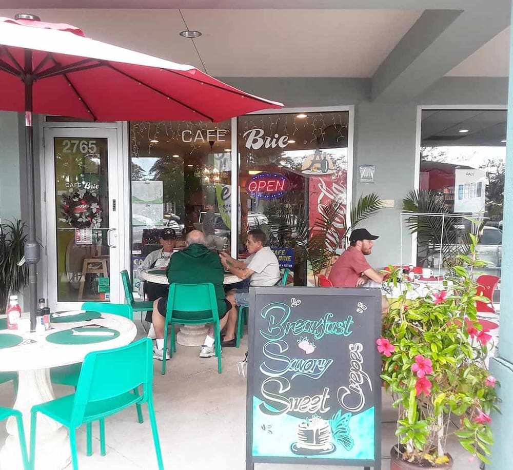 Outdoor dining at QuestForDirections café with vibrant teal chairs and a welcoming "Breakfast, Savory, Sweet, Crepes" sign.