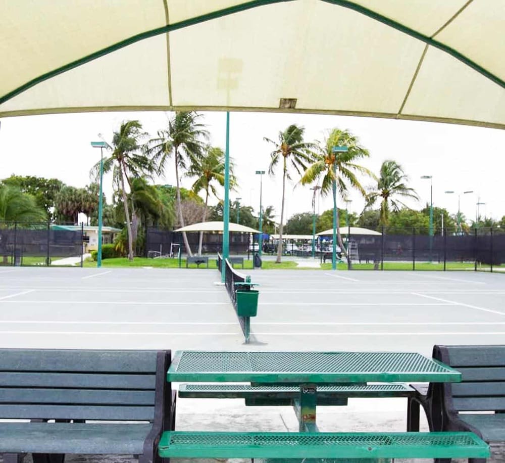 Tennis courts with palm trees and shaded seating area at Quest for Directions park in Florida.