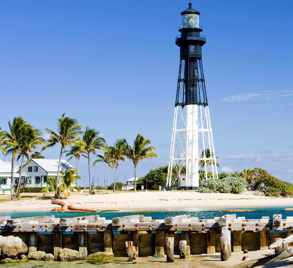 Lighthouse on tropical beach with palm trees and clear blue sky, perfect for seaside navigation.