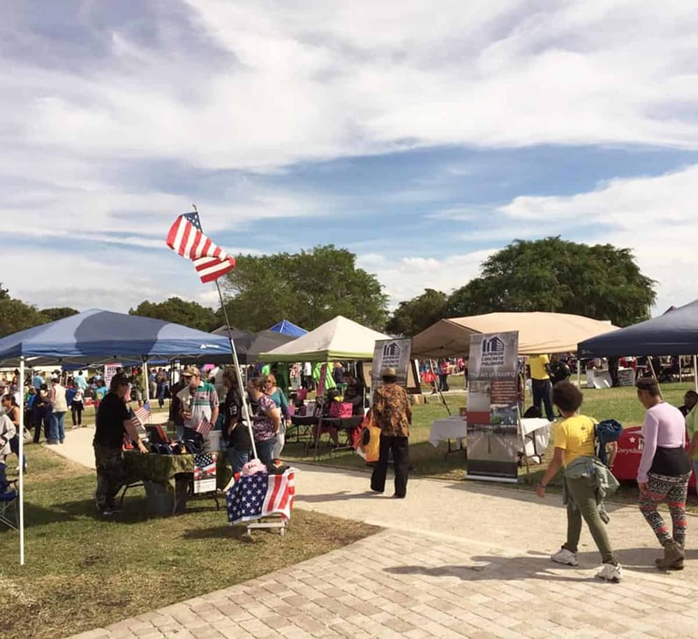 American flag at outdoor community event with vendor booths and attendees.
