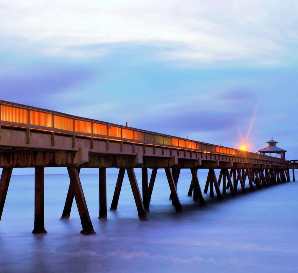 Pier at sunset with warm glow, ocean view, tranquil waters, and cloudy sky, perfect for seaside relaxation and scenic walks.