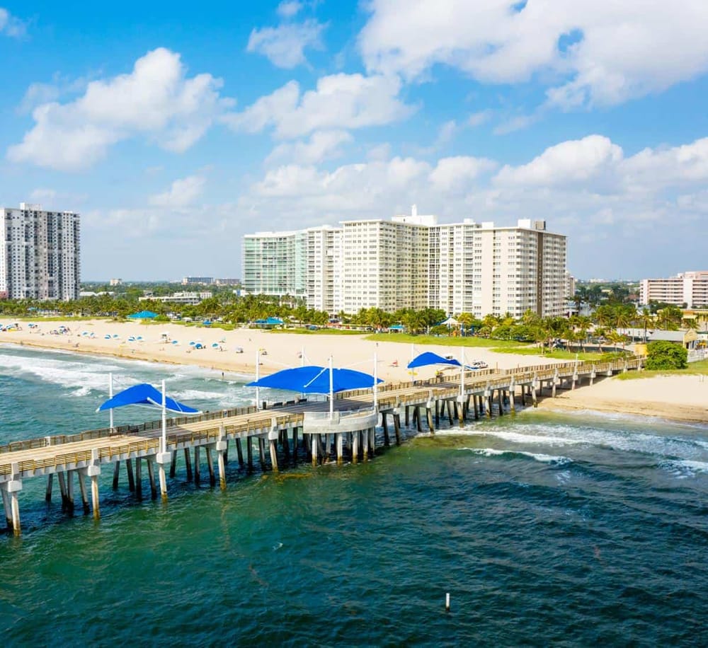 Beachside pier with umbrellas and modern beachfront hotel in sunny ocean resort destination.