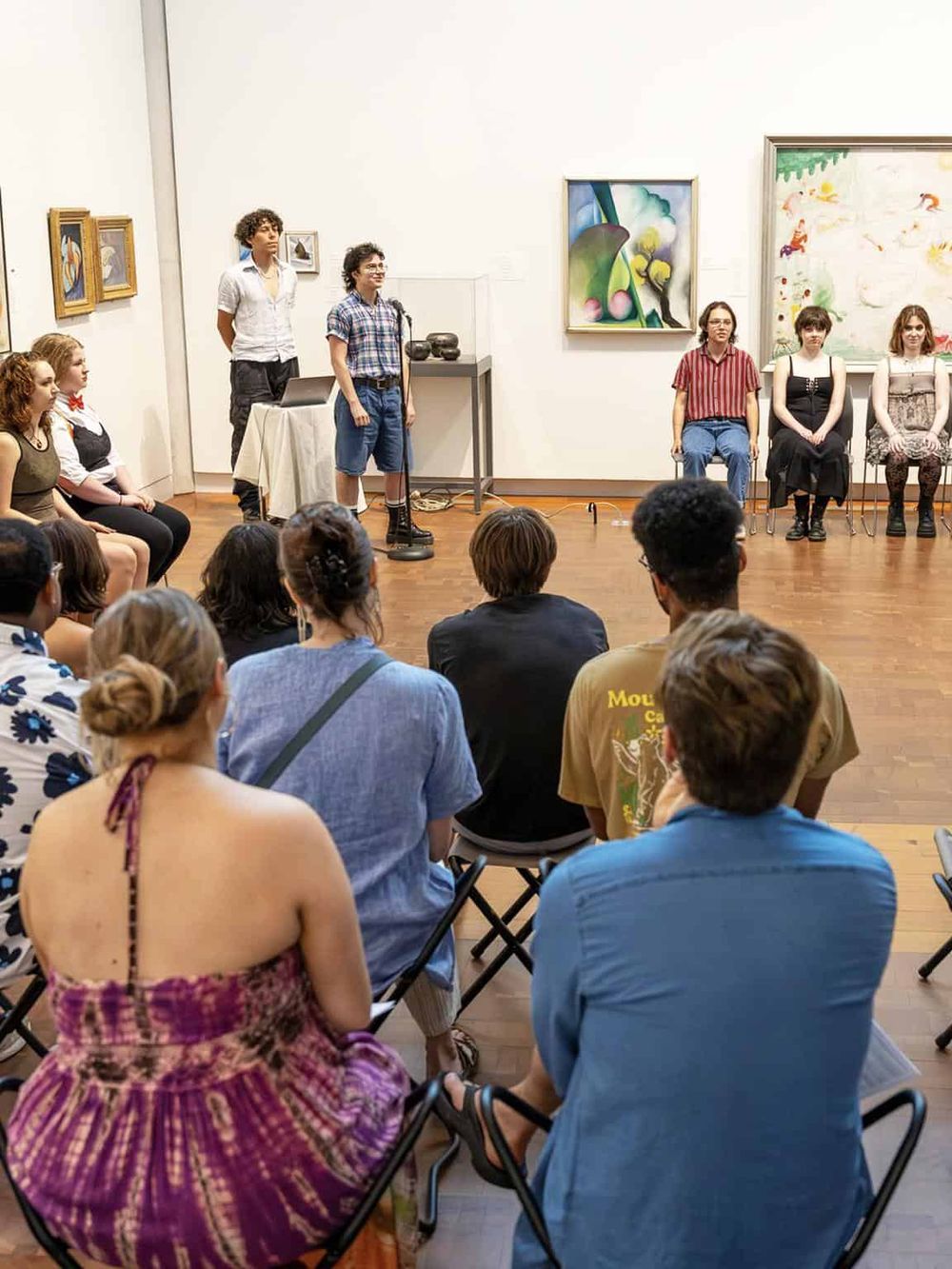 Teenagers performing a play in an art gallery, engaging an audience of diverse spectators.