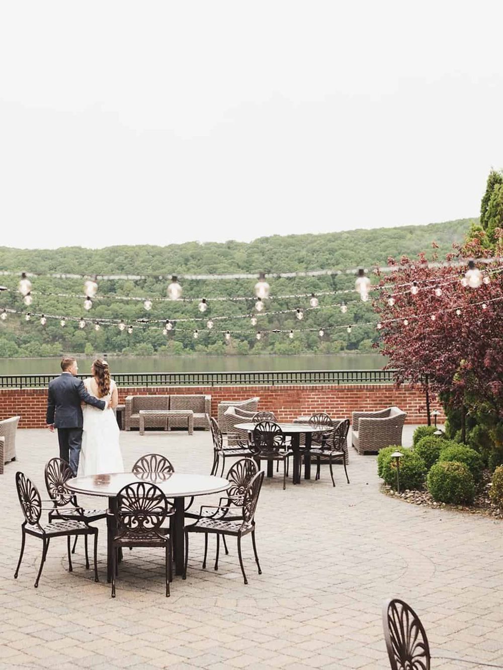 Elegant outdoor wedding venue overlooking a scenic river with string lights and lush greenery.