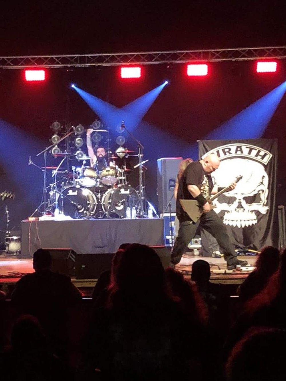 Vibrant live music performance featuring a drummer and guitarist on stage with stage lighting and a pirate-themed backdrop.