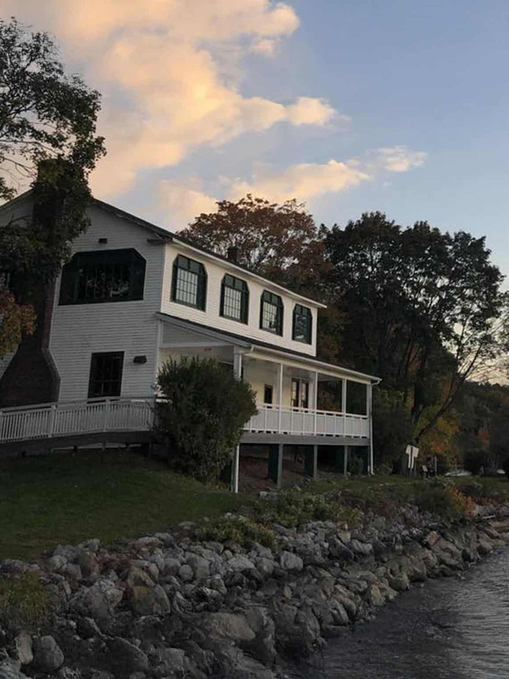 Coastal home overlooking water with trees and rocky shoreline, scenic view.