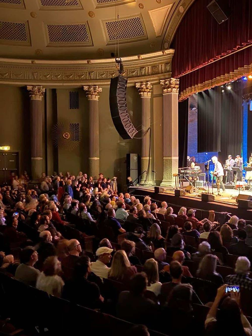 Elegant theater with live music performance, detailed architecture, and a full attentive audience.