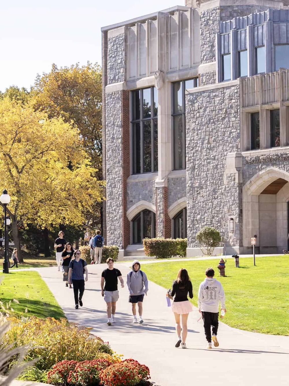 Students walking on college campus near historic building, autumn trees background, QuestForDirections service focus.