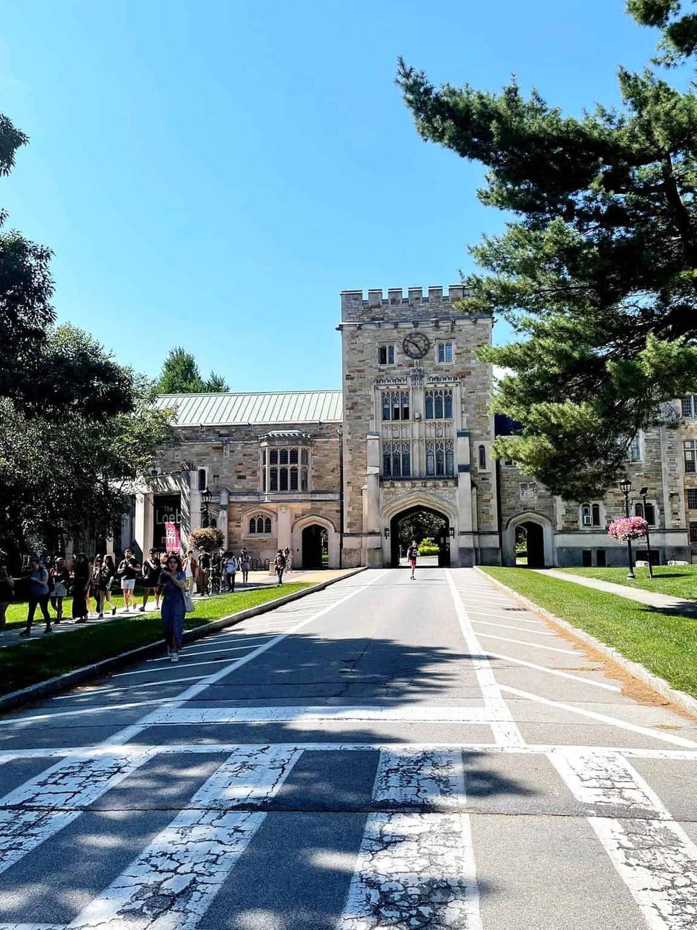 Historic university campus gateway with people, trees, and clear blue sky - QuestForDirections.
