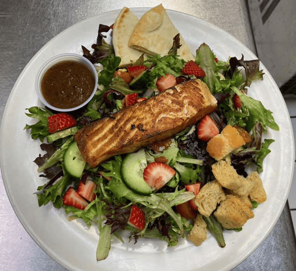 Grilled salmon salad with fresh strawberries, cucumbers, mixed greens, tortilla chips, and dressing.