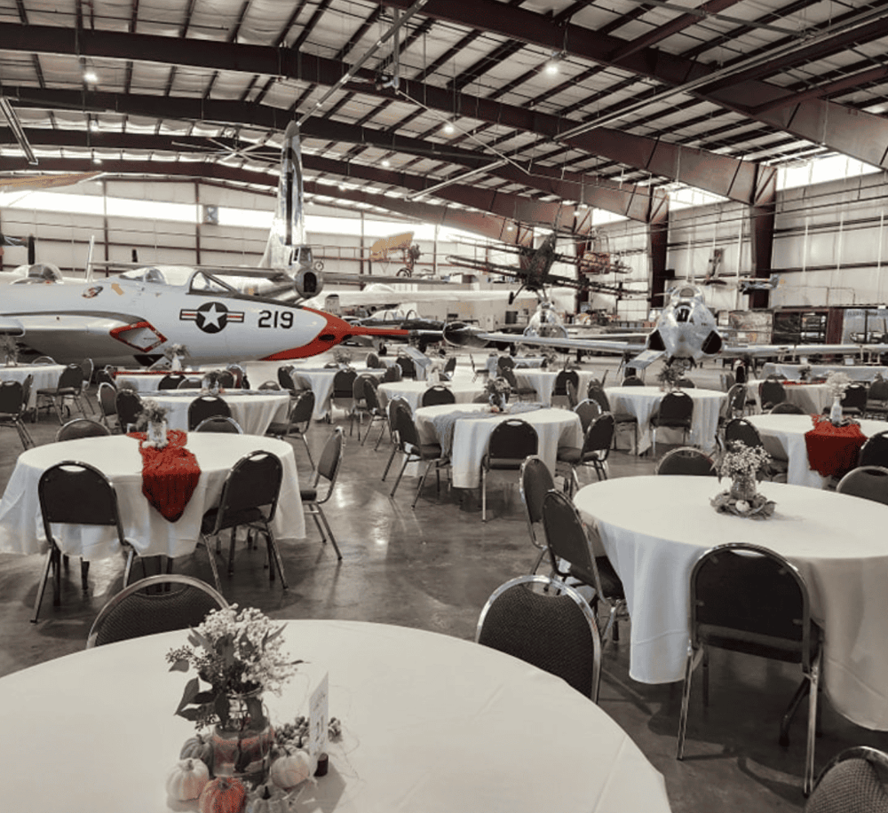Aircraft museum with banquet tables and festive decor inside an airplane hangar.