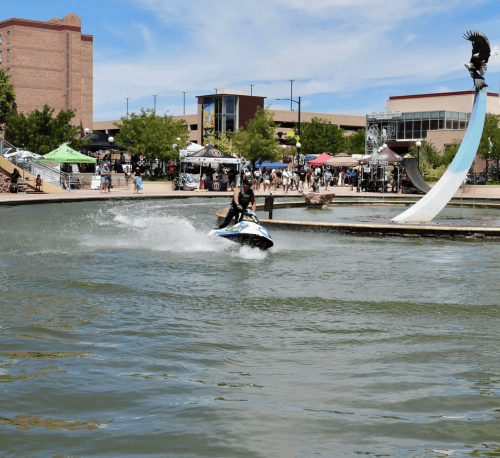 Jet ski rider on a water fountain at Quest for Directions outdoor plaza, bustling with visitors and vibrant city life.