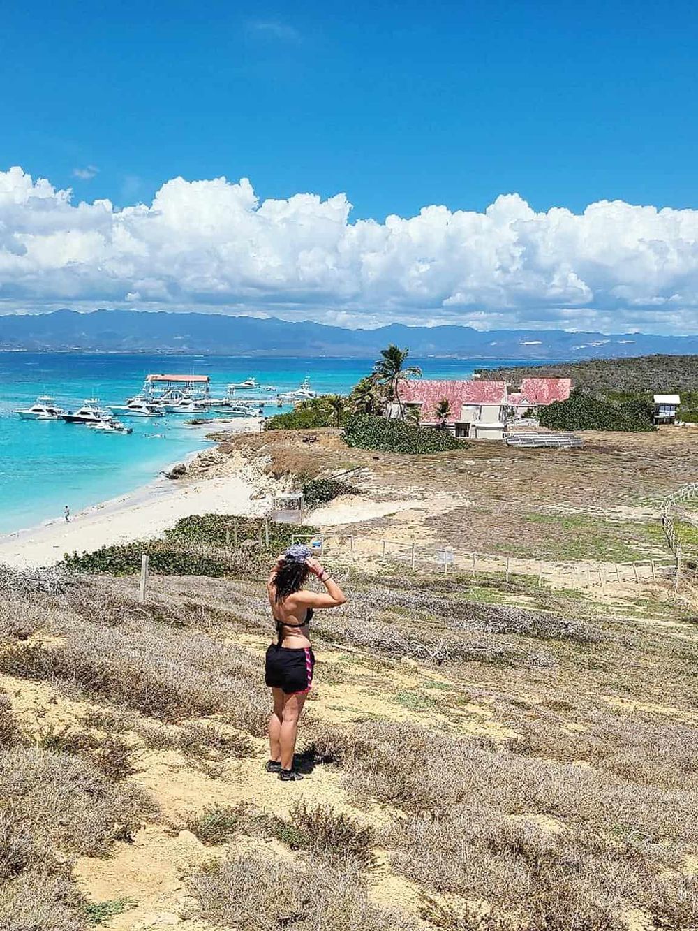 Seaside landscape with boats, woman taking photos, coastal homes, and mountains, perfect for adventure and travel keywords.