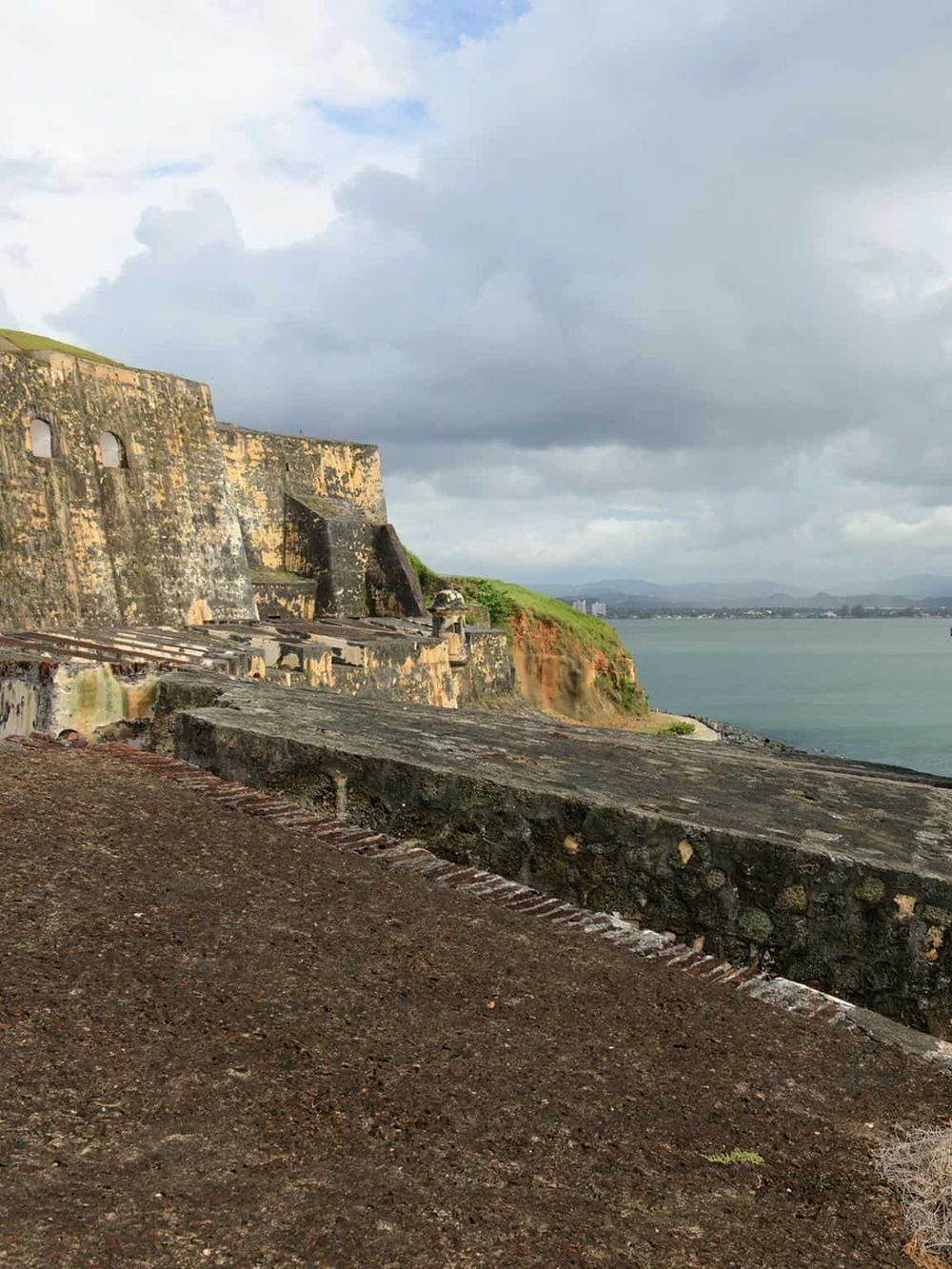 Ancient seaside fortress with stone walls overlooking the ocean, scenic coastal landscape, and cloudy sky.