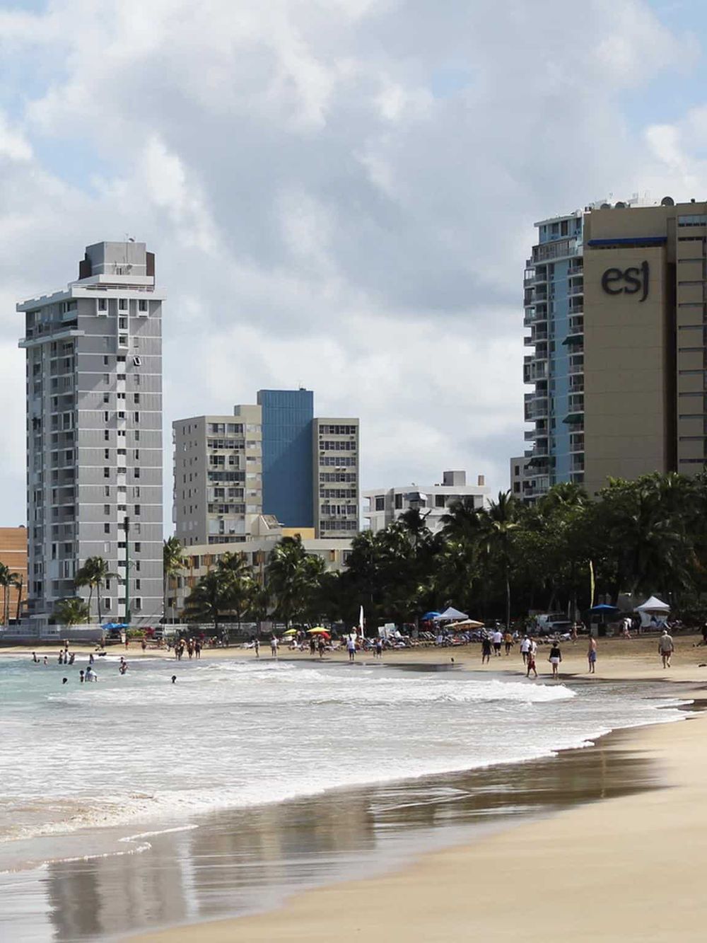 High-rise buildings along a sandy beach with people swimming and relaxing, showcasing urban coastal scenery.