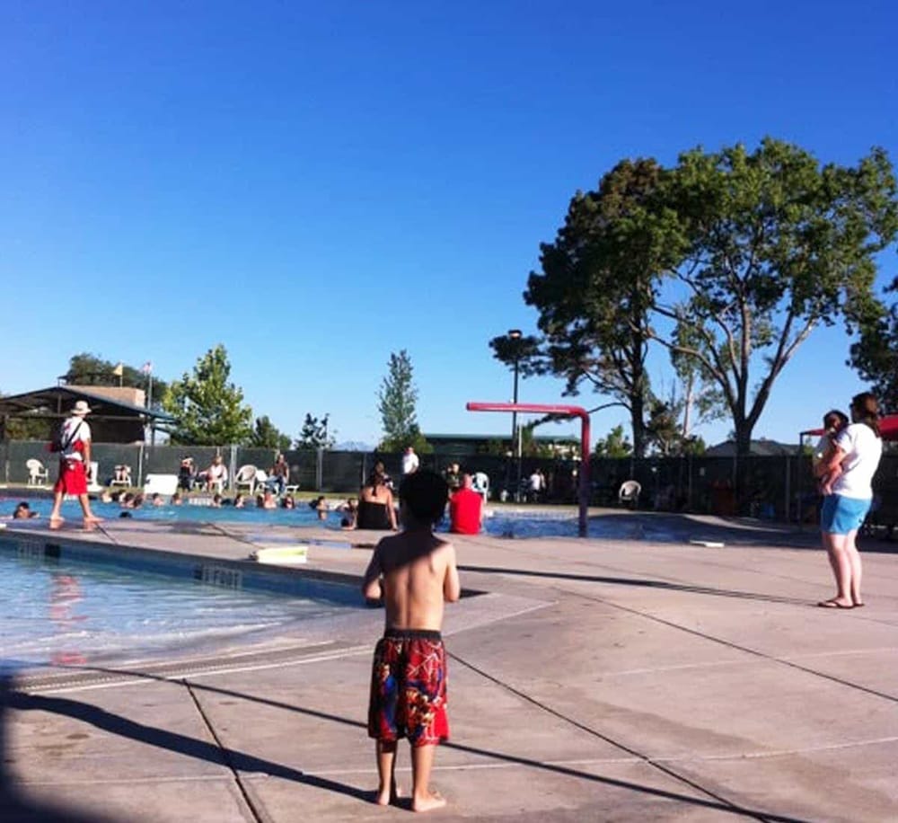 Children enjoying a summer day at an outdoor swimming pool with clear blue skies.