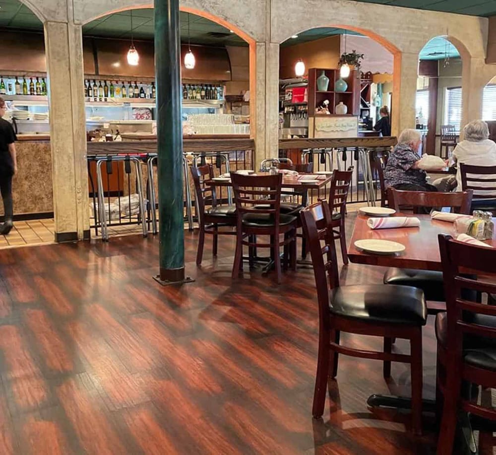 Cozy restaurant interior with wooden tables and chairs, welcoming atmosphere, and glimpses of customers dining.