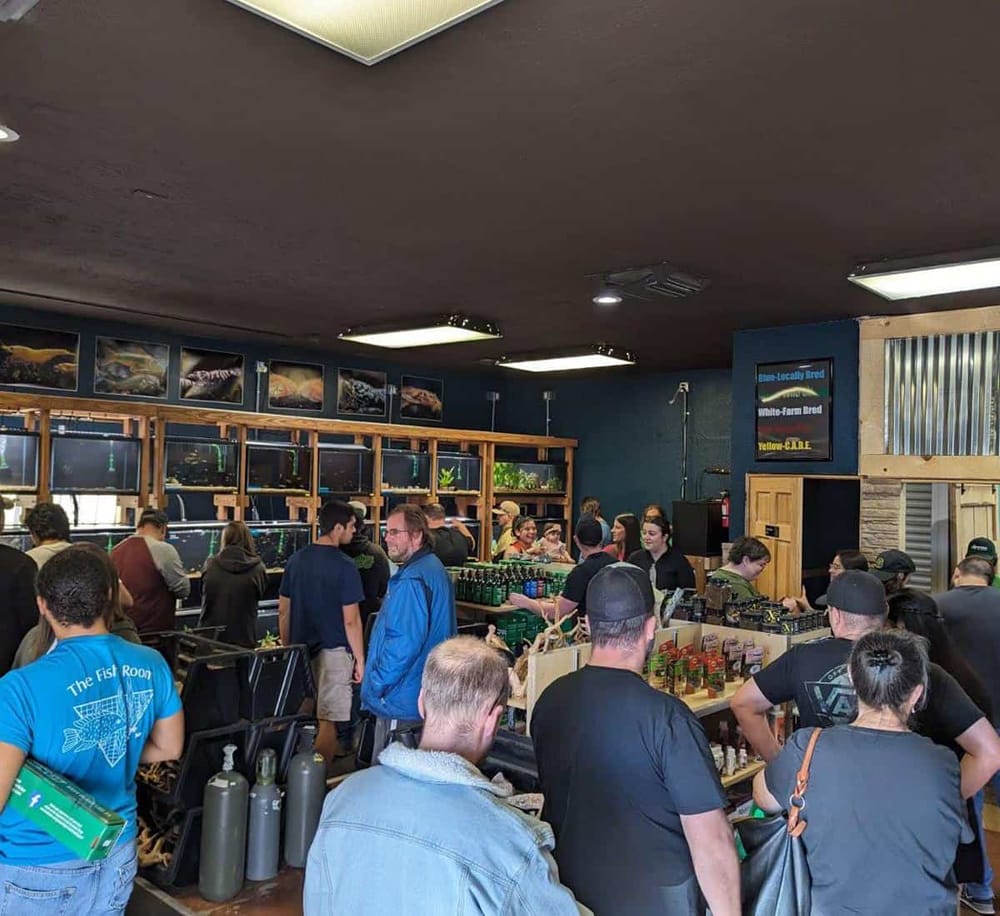 Vibrant indoor fishing store filled with shoppers browsing fish tanks and fishing gear, lively atmosphere and friendly staff.