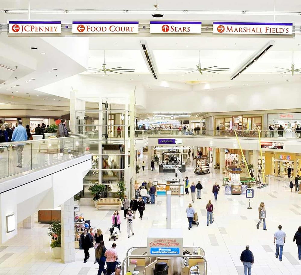 Bright shopping mall interior with directional signs for JCPenney, Food Court, Sears, and Marshall Field's.