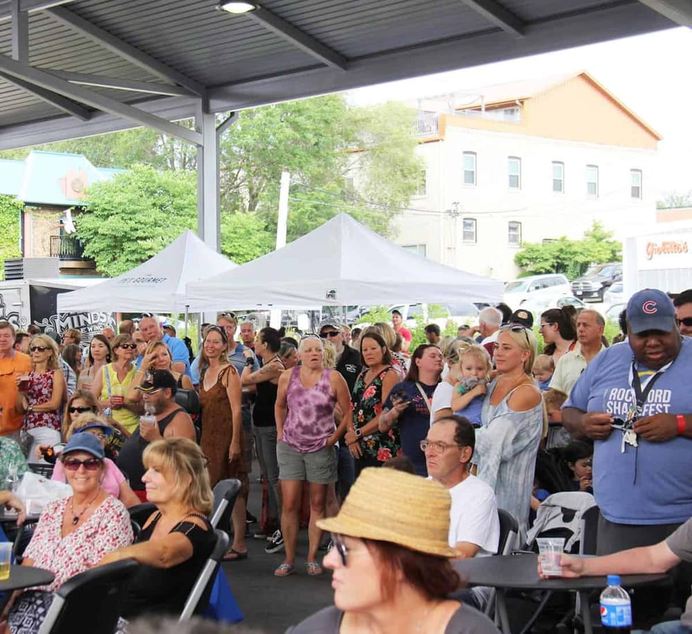 Crowd at a music festival under an outdoor pavilion, lively atmosphere, diverse attendees enjoying the event.