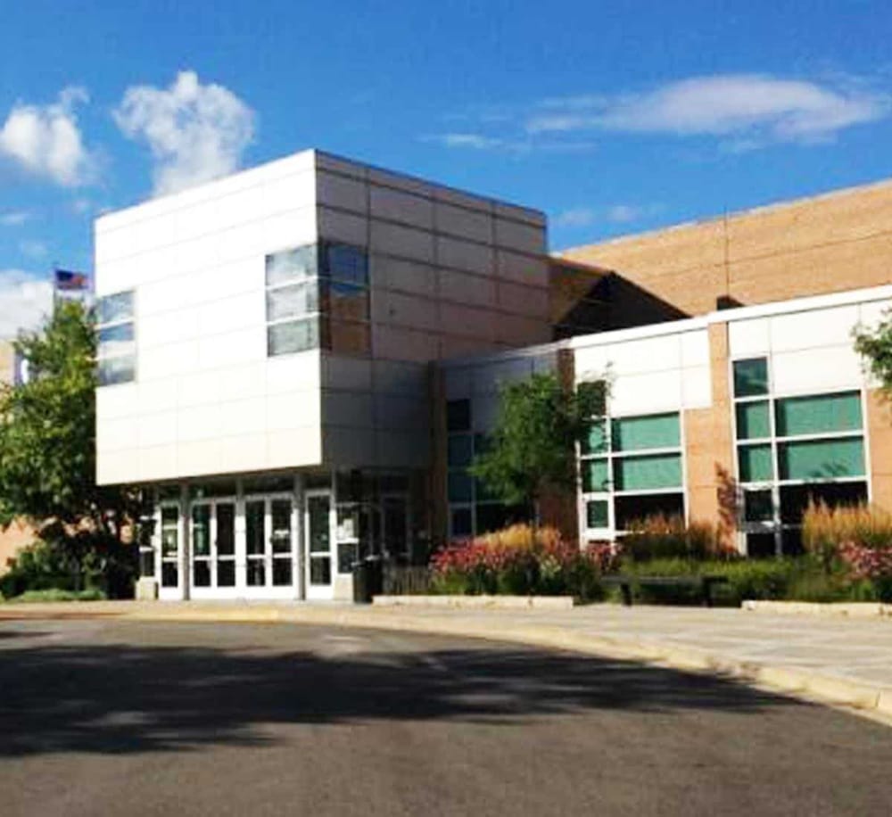 Modern educational building with glass windows and landscaped surroundings, located in a sunny area.