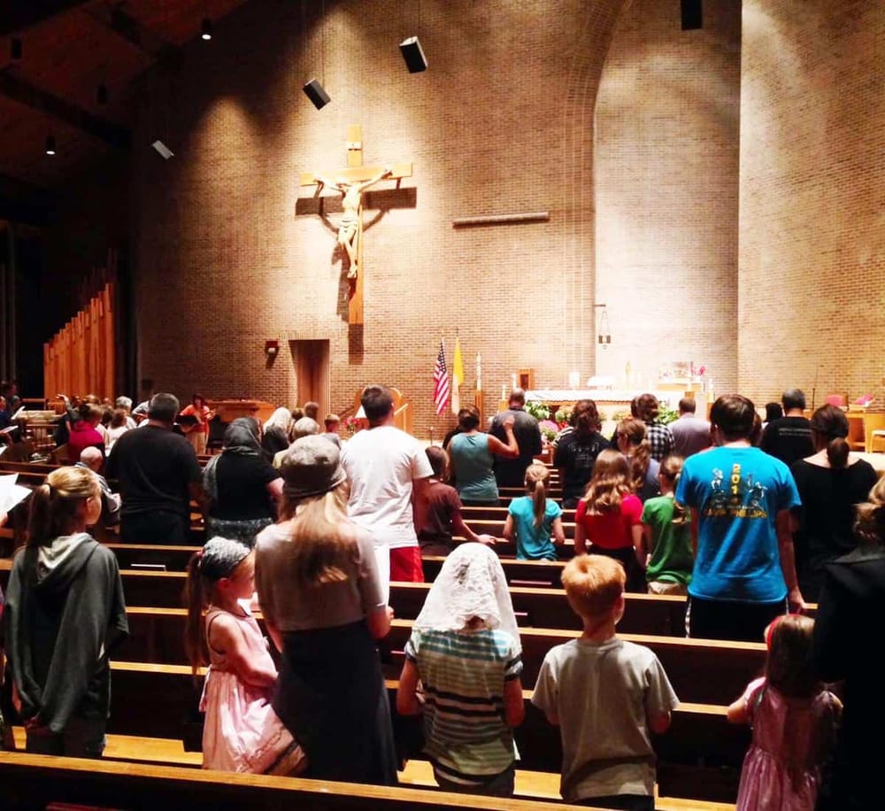 People attending a Catholic church service at the altar with crucifix on brick wall.