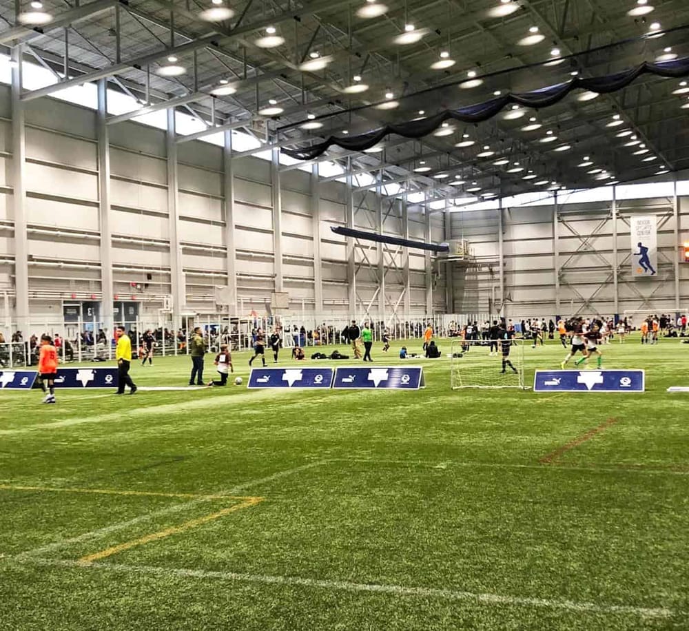 Indoor soccer training at QuestForDirections facility with players and coaches on a large field.