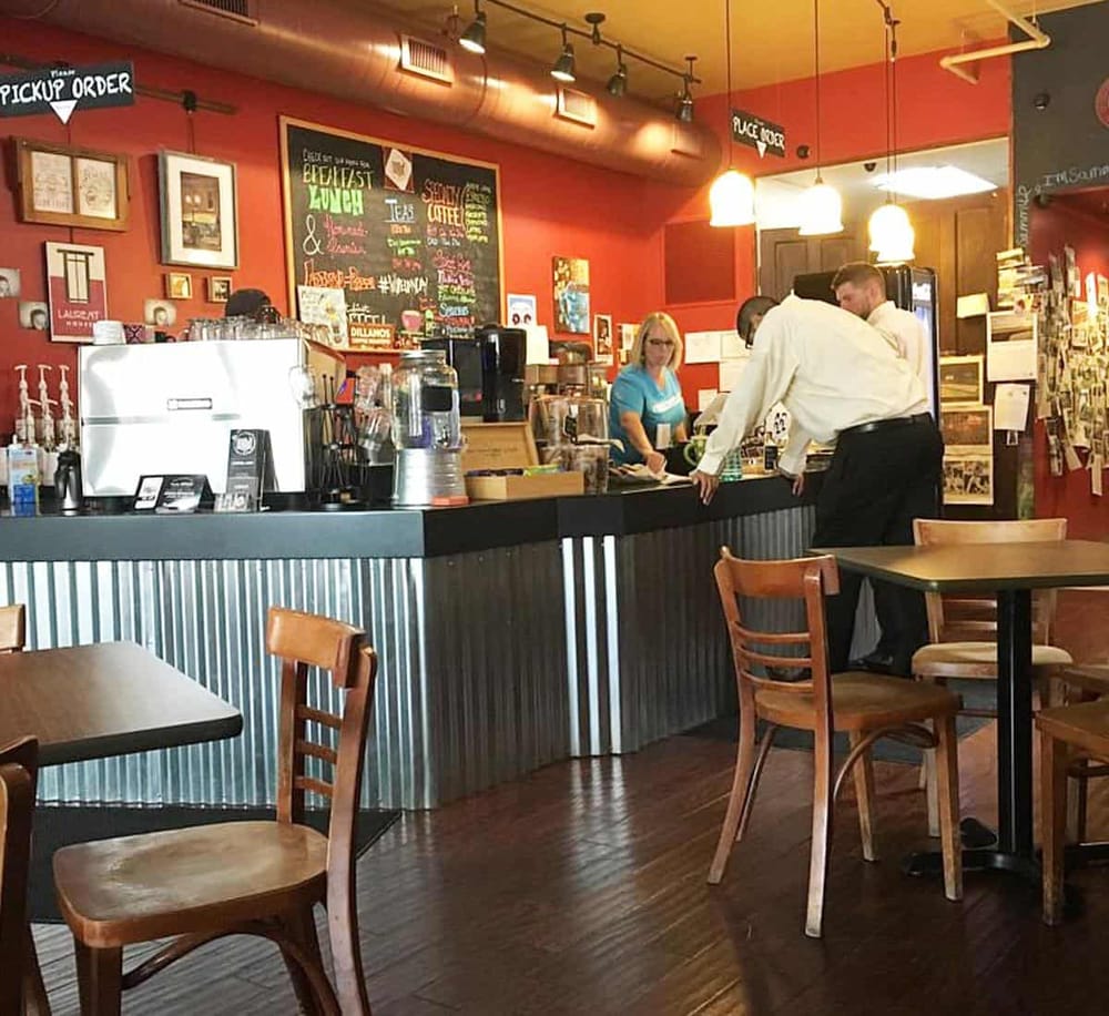 Cozy cafe interior with barista at counter and customer ordering coffee, warm lighting, and vibrant decor.