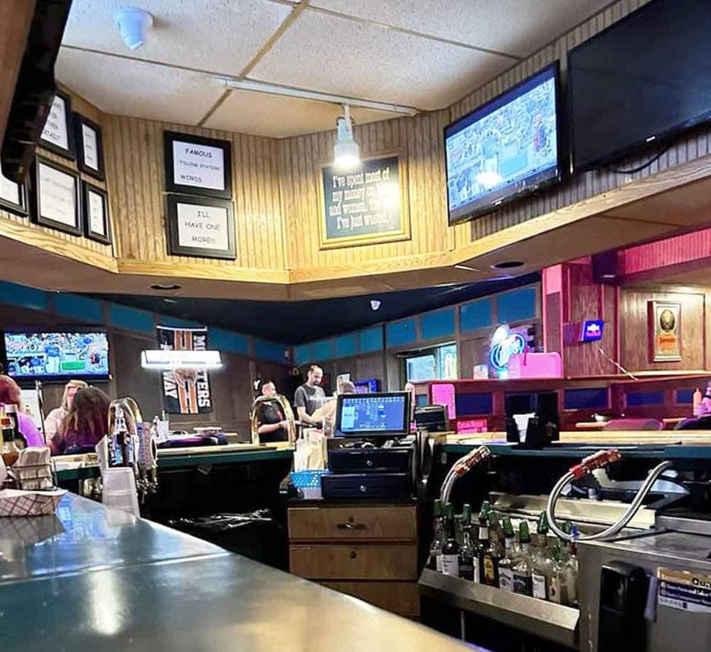 Crowded bar with multiple TVs, bartenders, and patrons enjoying drinks, creating a lively social atmosphere.