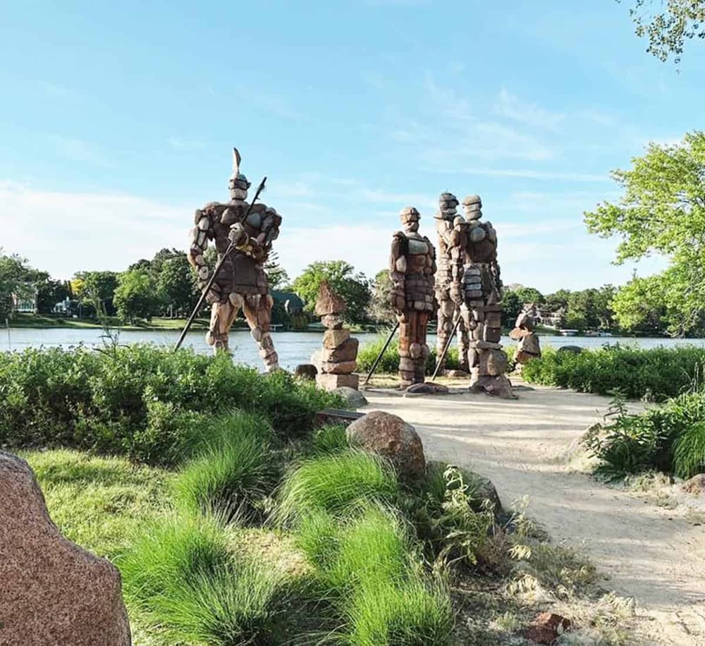 Viking warrior sculptures along a serene lakeside park, emphasizing outdoor exploration and adventure.