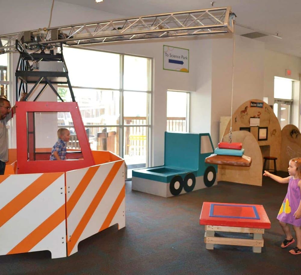 Colorful indoor children's play area with a mini construction crane and truck-themed seating at QuestForDirections.